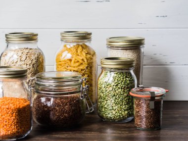 Çeşitli tahıllar ve tohumlar - pirinç, makarna, yulaf ezmesi, keten, mercimek, yeşil bezelye mutfakta masada cam kavanoz bölünmüş