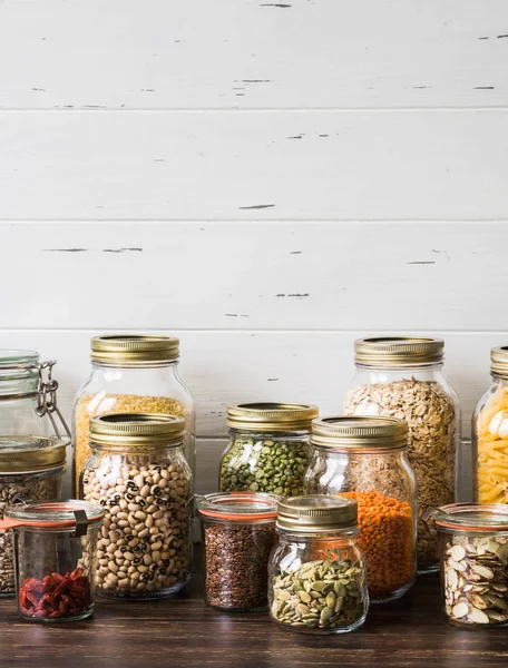 Diverses céréales et graines - pois cassés, graines de tournesol et de citrouille, haricots, riz, pâtes, flocons d'avoine, couscous, lin, amandes, lentilles, goji, bulgur dans des pots en verre sur la table dans la cuisine — Photo