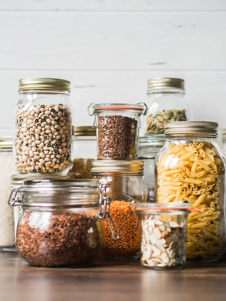 各种谷物和种子 - 南瓜籽，豆类，大米，意大利面，亚麻，扁豆，杏仁片，在厨房桌子上的玻璃罐的凸起 — 图库照片