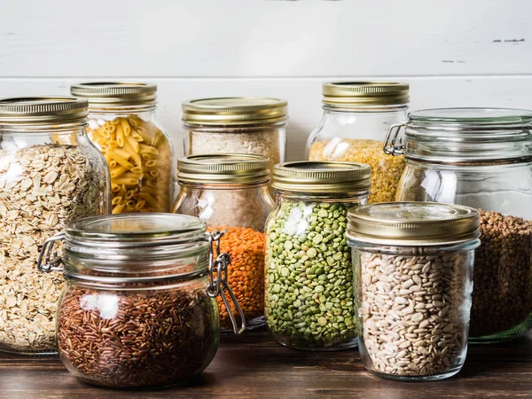 Çeşitli tahıllar ve tohumlar - bezelye bölünmüş, ayçiçeği tohumu, pirinç, makarna, yulaf ezmesi, kuskus, mercimek, karabuğday, mutfakta masada cam kavanoz bulgur
