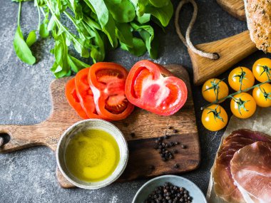 Sandviç yapmak için çeşitli taze malzemeler - sebze - domates ve arugula, ekmek, prosciutto, koyu arka plan üzerinde zeytinyağı. Üstte görüntü