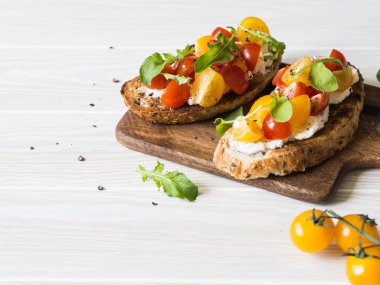 Krem peynir ve taze arugula ve zemin karabiber ile çeşitli renklerde taze domates dilimleri ile ızgara tost çifti ahşap bir kesme tahtası üzerinde