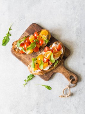 Krem peynir ve taze arugula ve zemin karabiber ile çeşitli renklerde taze domates dilimleri ile ızgara tost çifti ahşap bir kesme tahtası üzerinde