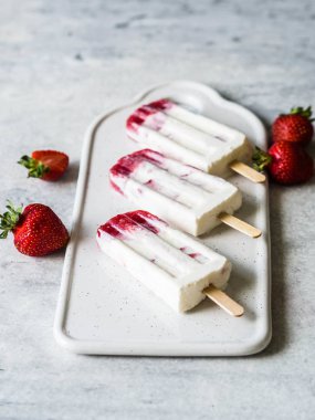 Gri bir arka plan üzerinde seramik bir tahta üzerinde taze çilek ve yoğurt popsicle