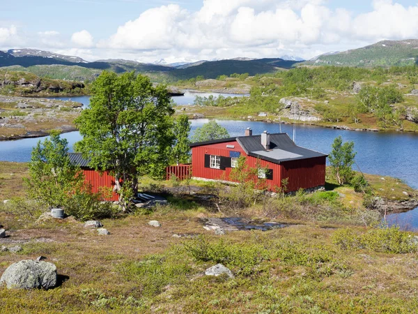 Traditionellt rött trä norskt hus vid sjön omgiven av klippor och berg — Stockfoto