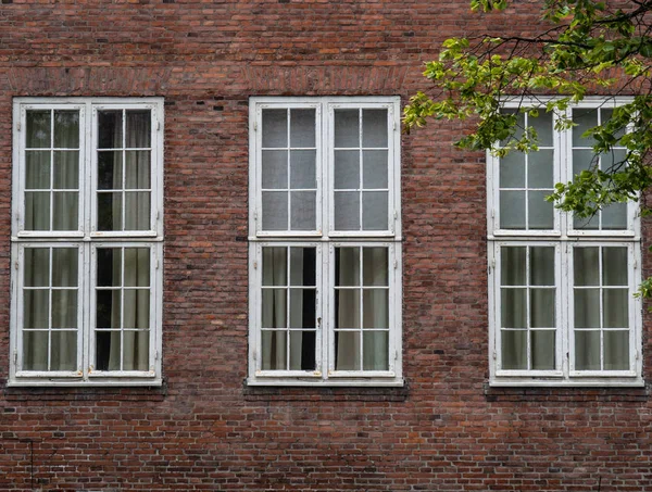 Tre stora rektangulära fönster med vita metallstänger på fasaden av ett gammalt tegelhus — Stockfoto