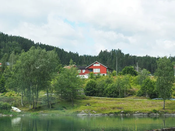 Tradicional casa norueguesa de madeira vermelha junto ao lago rodeado por montanhas e florestas — Fotografia de Stock