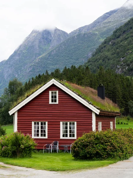 Casa tradicional de madera roja con plantas y césped en el techo. Casa en un valle verde cerca de una gran montaña — Foto de Stock