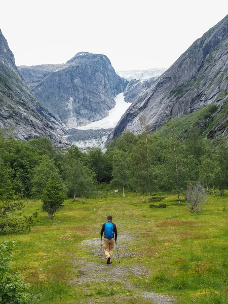 Un hombre indefinido con t va al lado de un glaciar a través de un valle en Noruega. Una de las ramas del glaciar Nigardsbreen, la vista desde el valle y el turista, viene con bastones de senderismo — Foto de Stock