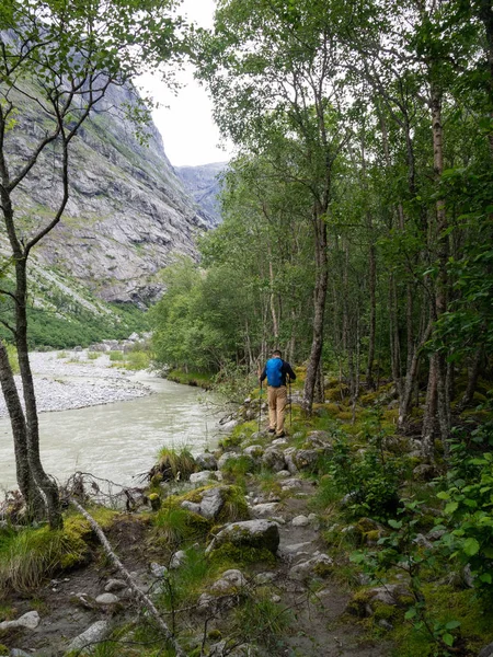 Un hombre indefinido con equipo turístico está caminando sobre piedras en un bosque en Noruega. Sendero a través del bosque junto a un río de montaña y piedras cubiertas de musgo — Foto de Stock