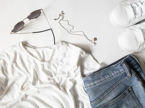T-shirt blanc bleu jeans, lunettes de soleil, collier et baskets blanches sur fond blanc. Tenues décontractées de femme allongée plate. vue de dessus — Photo