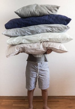 Belirsiz adam beyaz duvara karşı çeşitli renklerde büyük yastıktutar