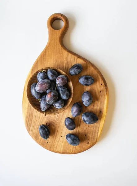 Prunes mûres bleues plein bol en bois sur une planche en bois sur un fond blanc vue de dessus — Photo