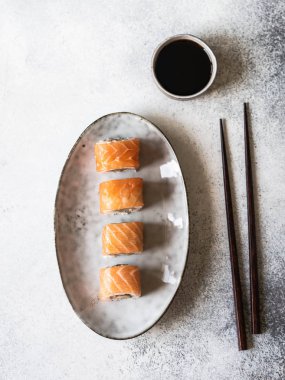 Gri arka planda oval seramik tabakta somon balıklı suşi rulosu. Üst görünüm