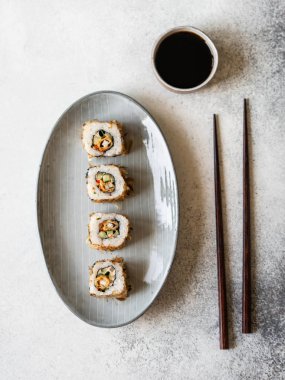 Deniz levreğiyle suşi rulosu ve oval seramik tabakta ton balığı cipsi. Üst görünüm