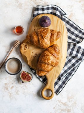 Tahta kesme tahtasının üzerinde kruvasanlar, gri arka planda incir ve espresso kahvesiyle kahvaltı.,