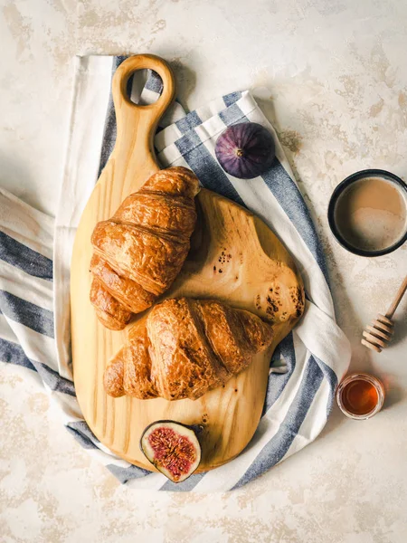 Tahta kesme tahtasının üzerinde kruvasanlar, gri arka planda incir ve espresso kahvesiyle kahvaltı.,