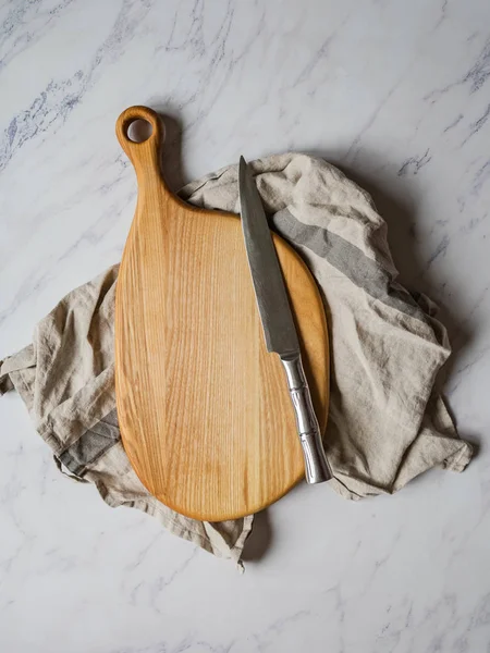 Tabla de cortar de madera en servilleta de cocina y cuchillo de metal sobre un fondo gris — Foto de Stock