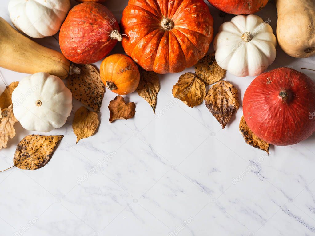 Pumpkins border of various sizes and colors and different dry autumn leaves on a marble background Top view. Copy space