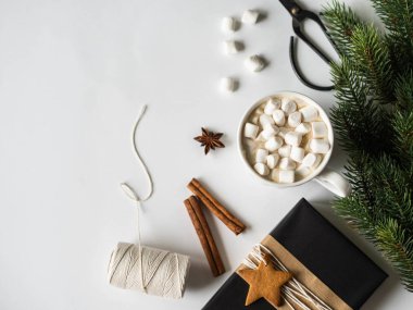 Baharatlı, marşmelovlu ve köknar dallı beyaz kupa ve beyaz arka planda siyah kağıtta sunuluyor. Üst Manzara. Boşluğu kopyala