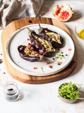 Fırında patlıcan dilimleri, baharatlar, lahanalar, nar yağları ve gri arka planda beyaz seramik bir tabakta..