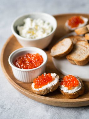 Krem peynirli sandviçler ve büyük ahşap tepside kırmızı havyar ve kaselerdeki malzemeler.
