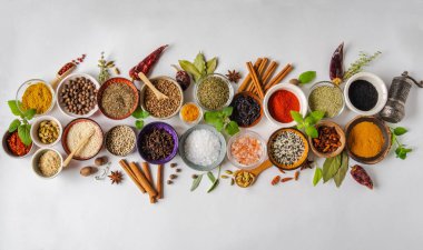 Küçük kaselerde çeşitli kuru baharatlar ve beyaz arka planda düzleşmiş çiğ otlar vardı. Üst görünüm,