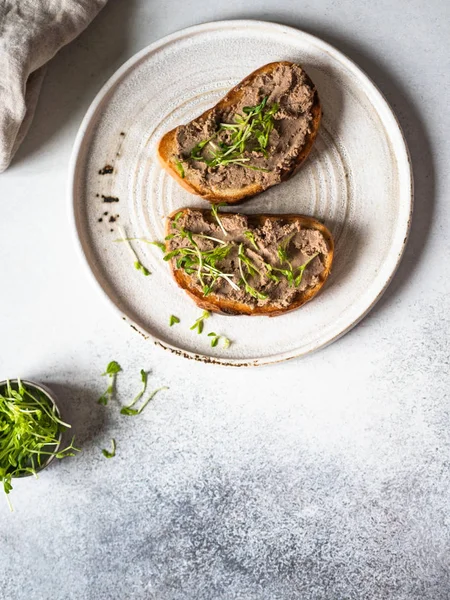 Deux rillettes de poulet grillées (pâté) sur du pain blanc avec des germes sur une assiette blanche sur un fond clair. Vue du dessus — Photo