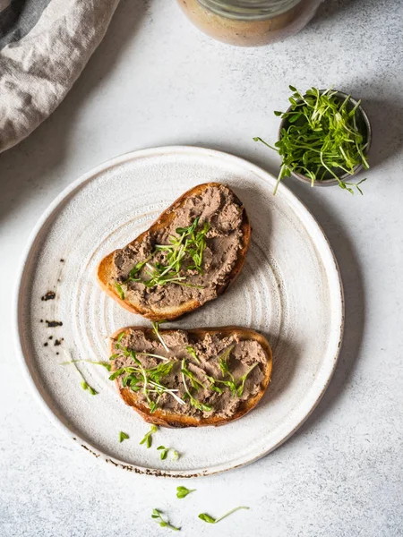 Deux rillettes de poulet grillées (pâté) sur du pain blanc avec des germes sur une assiette blanche sur un fond clair. Vue du dessus — Photo