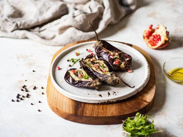 Berenjenas al horno rebanadas con especias, brotes, granada y aceite de oliva en un plato de cerámica blanca sobre fondo gris . —  Fotos de Stock