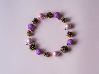 Pembe arka planda çember şeklinde çeşitli noel topları ve koniler.