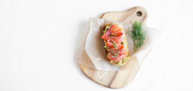 Tahtadaki beyaz kağıtta avokado ve füme somon tostu. Sağlıklı yemek afişi. Üst Manzara. Boşluğu kopyala