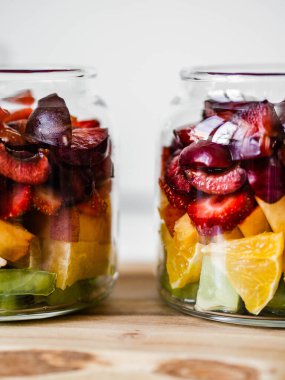 Böğürtlen ve meyveli iki cam kavanoz. Kivili meyve salatası, şeftali, çilek, kiraz ve ahşap kavanozlarda erik. Yaz mevsimsel lezzetli vejetaryen salatası atıştırmalık ya da öğle yemeği için