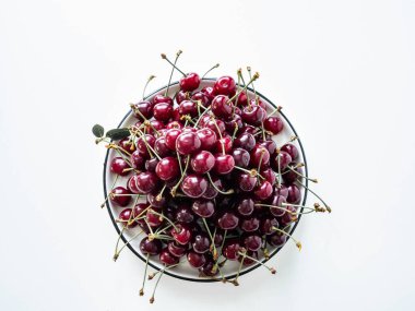 Beyaz arka planda beyaz tabakta yaprakları olan büyük olgun kiraz meyveleri. Üst Manzara. Boşluğu kopyala