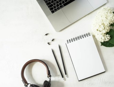 Bilgisayarı, defteri, kalemleri, beyaz ortancaları ve beyaz arka planda kulaklıkları olan ofis masası çalışma alanı. Düzlük, üst görünüm kız iş dünyası yaşam tarzı blogu, sosyal medya konsepti.