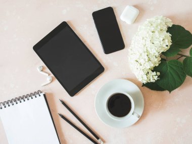Ofis masası çalışma alanı, siyah akıllı telefon, siyah tablet, fincanda kahve, beyaz ortanca, beyaz kulaklıklar ve pembe arka planda grafit kalemler. Düzlük, üst görünüm kız iş dünyası yaşam tarzı blogu konsepti