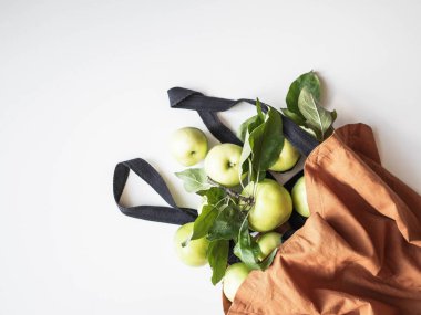 Beyaz arka planda pamuk kahverengi torbada yaprakları olan taze yeşil elmalar. Üst Manzara. Boşluğu kopyala