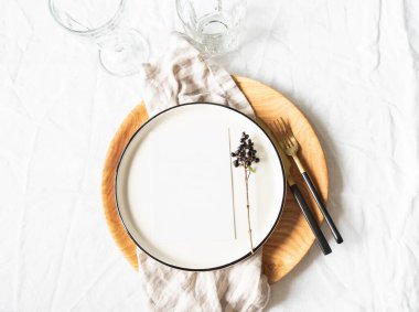 Servis masası için sofra takımı ve dekorasyonlar. Seramik ve ahşap tabaklar, şarap bardakları ve beyaz masa örtüsü üzerine keten peçete serpiştirilmiş çatal bıçak takımı. Üst görünüm.