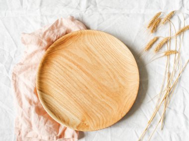 Yuvarlak ahşap tepsi ve beyaz tekstil arka planında kuru buğday kulakları. Üst Manzara. Boşluğu kopyala