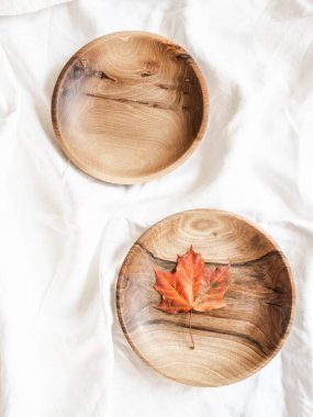 Beyaz pamuk masa örtüsü üzerinde kırmızı sonbahar yaprağı olan boş kahverengi yuvarlak ahşap kâse ve kâse manzarası. Düz yatıyordu. Sapı kopyala