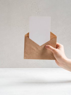 Kadın el ele tutuşup açık bir zarf ve gri arka planda bir kartpostal var. Boşluğu kopyala