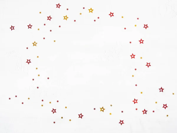 Christmas confetti stars frame. Flat lay of gold and red stars on a white background. Top view. Copy space