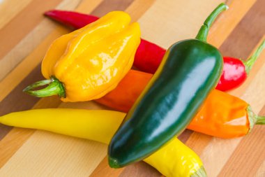 izole ahşap arka plan üzerinde kırmızı, yeşil, sarı ve turuncu biber