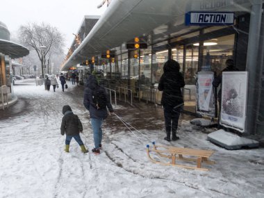 Lahey, Hollanda - 10 Aralık 2017: kızak ile alışveriş merkezi yakınında karla kaplı sokakta yürüyen çocuk grubu