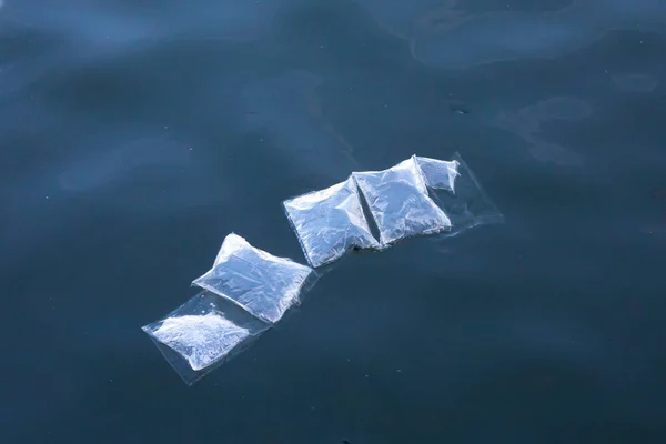 plastic marine pollution, underwater plastic bags and packaging floating semi submerged at surface of water