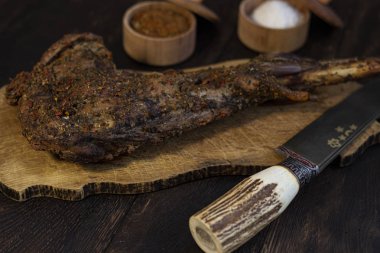 Baharat ve bıçak ile meşe masada Pişmiş keçi bacak