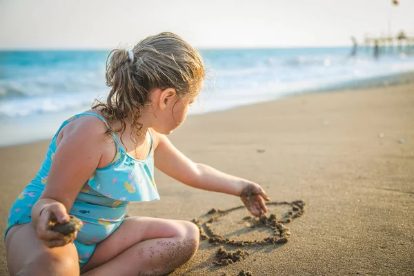 Küçük bir kız bir güneş kum deniz kenarında üzerinde çizer