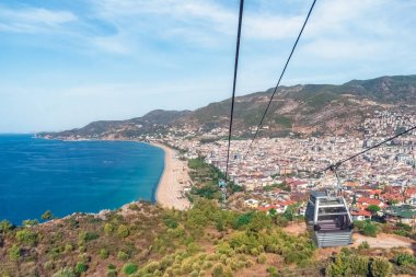 Türkiye 'nin Alanya kentinden Kleopatra Sahili' nin sahil şeridi boyunca uzandığı Alanya Teleferik teleferiğinden nefes kesici bir görüntü. Deniz, dağlar ve şehir manzarasının çarpıcı birleşimi unutulmaz bir manzara yaratır.