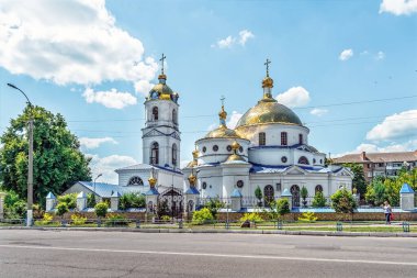 Romny 'deki Yükseliş Kilisesi' nde beyaz duvarlar, altın kubbeler ve mavi gökyüzünde Ortodoks haçları olan çan kulesi yer alıyor. Yeşil ağaçlar ve mavi çitlerle çevrili geleneksel Ukrayna dini mimarisi. Romny, Ukrayna - 29 Haziran 2024