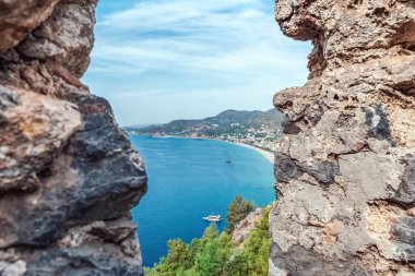 Akdeniz, Türkiye 'deki Alanya Şatosu' nun antik taş duvarlarından görüldüğü gibi. Bu perspektif, tarihi kalıntıların çerçevelediği sahilin güzelliğini vurgular.